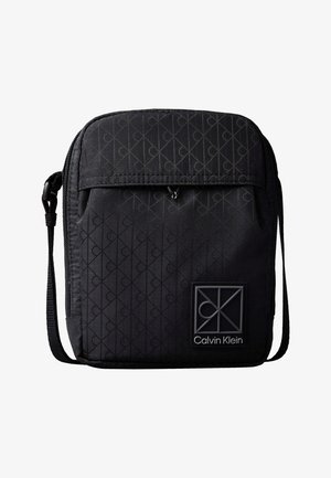 Μαύρη τσάντα Calvin Klein χιαστί με ρυθμιζόμενο λουράκι, μπροστινή τσέπη με καπάκι, διακριτικό μοτίβο μονόγραμμα και ετικέτα με το λογότυπο της μάρκας.