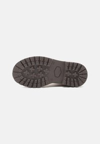 Semelle de chaussure en caoutchouc noir avec un motif de bande de roulement texturé comportant plusieurs sections surélevées et des détails hexagonaux pour une meilleure adhérence.