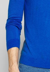 Royalblå tröja i mjukt stickat tyg. Har ribbade muddar och fåll. Tightly fit med en slät yta och inga synliga mönster.