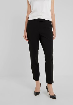 Svarte skreddersydde bukser med slim fit og ankel-lengde, laget av glatt stoff. Kombinert med svarte spissede hæler og en hvit topp.