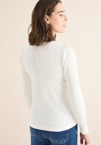 Witte geribde longsleeve top van zacht materiaal. Beschikt over een ronde halslijn en aansluitende mouwen, gecombineerd met blauwe denim jeans.