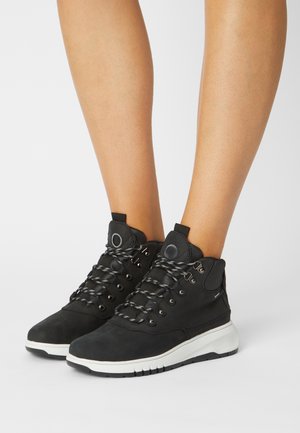 Botas de hiking pretas com acabamento suave, apresentando um design de atacadores, ilhós metálicos, um colar acolchoado e uma sola de borracha branca.