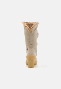 Botín de ante beige hasta el tobillo con un forro de piel de imitación marrón texturizado, un tacón ligeramente acampanado y una cremallera lateral para el cierre. Destacado con una pequeña hebilla.