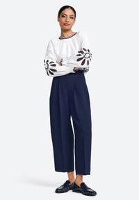 Blusa bianca con ricami floreali sulle maniche, abbinata a pantaloni navy a gamba larga e scarpe in pelle verniciata nera.