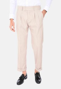 Pantaloni plissettati color beige chiaro con vita a due bottoni, polsini arrotolati in modo ordinato e una superficie liscia, abbinati a mocassini neri.