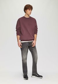 Maroon Sweatshirt mit Rundhalsausschnitt, kombiniert mit grauen Jeans und schwarzen Turnschuhen. Lässiger Schnitt, einfarbig, minimalistisches Design.