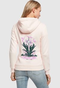 Felpa rosa chiaro con cappuccio regolabile, caratterizzata da una grafica di mani ed elementi geometrici in verde scuro e rosa sul retro.