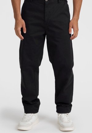 Schwarze Baumwollhose mit geradem Bein, ausgestattet mit Fronttaschen, einem Knopfverschluss und einer glatten Textur. Getragen mit weißen Sneakers.