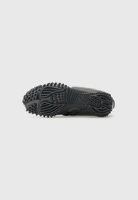 Mustade sneakersite välispind on tekstureeritud kummist tread, millel on sügavad sooned ja ümmargused haardepunktid, et tagada haardumine. Sile ülemine äär ilma nähtava brändimiseta.