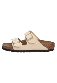 Beige suede sandals with two adjustable straps and silver buckles. Cork footbed on a textured black rubber outsole. Open-toe design.
