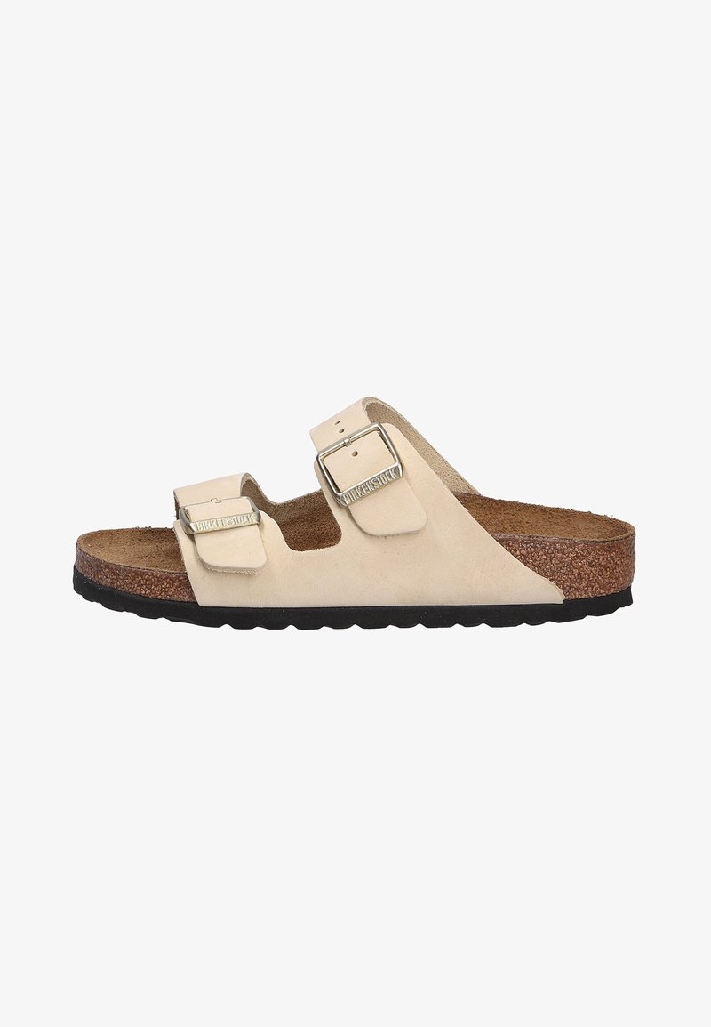 Beige suede sandals with two adjustable straps and silver buckles. Cork footbed on a textured black rubber outsole. Open-toe design.