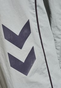 Hellgrauer Stoff mit glatter Textur zeigt dunkelblaue Chevron-Muster. Ein schmaler, dunkler Saum verläuft entlang des Randes.