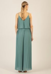Plissé maxi-jurk in zacht teal, met een gelaagd ontwerp, dunne bandjes en een V-rug. Lichtgewicht stof met een vloeiende textuur en een soepele afwerking.