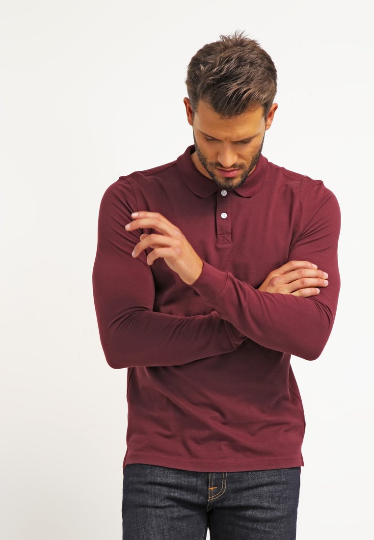 Camisa polo de manga larga burdeos con cuello, tapeta de tres botones y diseño ajustado, combinada con jeans oscuros.