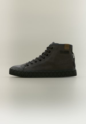 Zapatilla deportiva de caña alta de color gris oscuro con suela negra gruesa de goma, cordones y logo Palladium en el lateral sobre un fondo claro y liso.