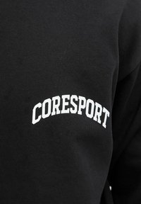 Hanorac negru cu text alb "CORESPORT" într-un design arcat. Materialul pare moale, cu o textură netedă. Stil simplu și minimalist.