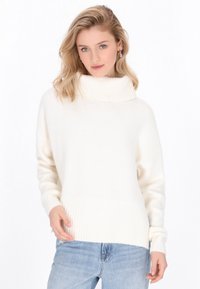 Weißer, gestrickter Pullover mit hohem Rippenkragen, gerippten Bündchen und Saum. Weiche Textur, lockerer Schnitt, kombiniert mit hellblauen Jeans.