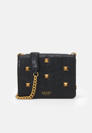 Black quilted leather crossbody bag with gold pyramid studs, gold chain strap, and "Guess EST 1981" logo on front.