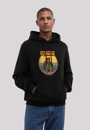Man wearing black hoodie with Yellowstone National Park design featuring a bear and two children in front of mountains and lake.