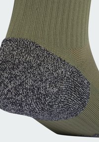 Calcetín verde de punto con talón texturizado en patrón negro y gris. El calcetín tiene un ajuste ceñido, superficie suave y costuras reforzadas.