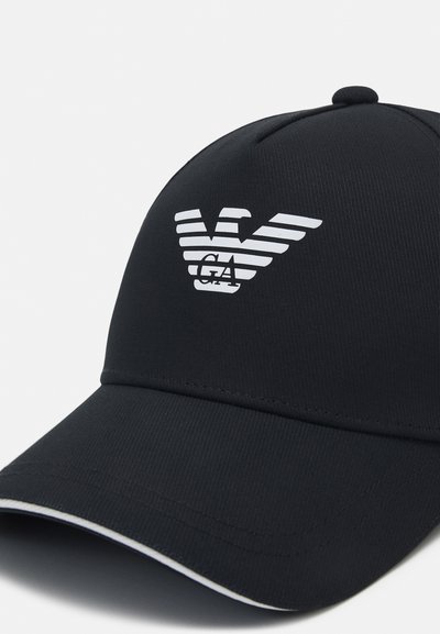 Casquette de baseball noire en tissu texturé avec un visière incurvée. Présente un logo d'aigle blanc et des rayures horizontales à l'avant.
