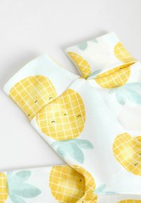 Bomullssockor med en ljusblå bakgrund som har gula ananaser och gröna blad; leende ansikten; mjuk textur och ankel-längd.