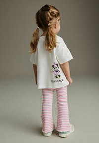 Weißes, übergroßes T-Shirt mit einem Minnie-Maus-Graphic in Pink und Schwarz, kombiniert mit pink-weißen, gestreiften Schlagleggings.