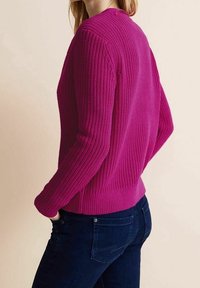 Fuchsia stickad tröja med ribbat mönster, rund halsringning och långa ärmar, med en åtsittande passform vid midjan och en enkel design.