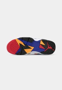 Suola di una sneaker con motivi geometrici neri, rossi, blu e gialli e un logo Jumpman rosso vicino al tallone.