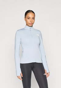 Ανοιχτό μπλε μπουφάν με φερμουάρ, ψηλό γιακά, μακριά μανίκια και εφαρμοστή γραμμή. Διαθέτει διακριτικό λογότυπο στο στήθος. Συνδυάζεται με μαύρα κολάν.