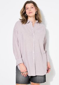 Camisa de botones a rayas en rosa claro y blanco, con cuello, mangas largas y un bolsillo en el frente, combinada con pantalones cortos de mezclilla oscura.