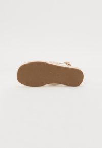 Beige sandal with a textured rubber sole and a minimalistic design. Features a single strap and metallic buckle for adjustable fit.