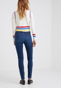 Bomullströja med röda, blå och gula horisontella ränder, matchad med mörkblå smala jeans och svarta klacksandaler.