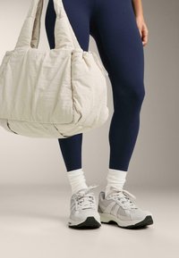 Lysebeige quiltet taske, marineblå leggings og grå sneakers med hvide detaljer. Sneakers har mesh og ruskindsstruktur med sort sål.