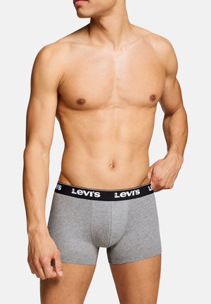 Hemdloser Mann richtet graue Levi’s Boxershorts mit schwarzem Bund vor einfachem weißem Hintergrund.