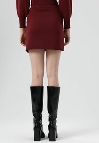 Mini-jupe bordeaux au design ajusté, accompagnée de bottes en cuir noir montantes jusqu'aux genoux, dotées d'un talon carré et d'une texture élégante.
