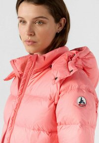 Giacca a vento rosa con colletto alto, bottoni a pressione e patch con logo sulla manica. Texture morbida e lucida con design trapuntato.