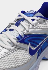 Άσπρο και μπλε παπούτσι running της Nike με πλέγμα στο πάνω μέρος, λευκά κορδόνια και εμφανές μπλε λογότυπο Nike στο πλαϊνό μέρος.