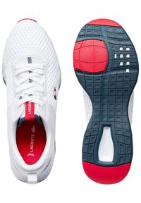 Baskets de sport en mesh blanc avec une semelle rouge et marine, dotées d'une épaisse semelle intermédiaire blanche, d'un système de laçage et du logo Lacoste sur le côté.
