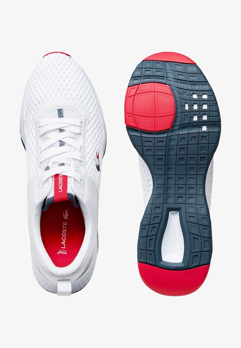 Baskets de sport en mesh blanc avec une semelle rouge et marine, dotées d'une épaisse semelle intermédiaire blanche, d'un système de laçage et du logo Lacoste sur le côté.