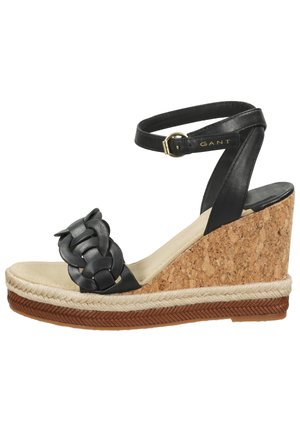Sandalias de cuña de cuero negro con un detalle de tira trenzada, tacón de corcho y una banda de yute natural alrededor de la suela. Acento de hebilla dorada.