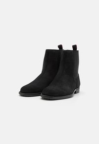 Bottines en daim noir avec panneaux latéraux élastiques, bout rond, et petit talon bloc. Dotées de languettes pour un enfilage facile.