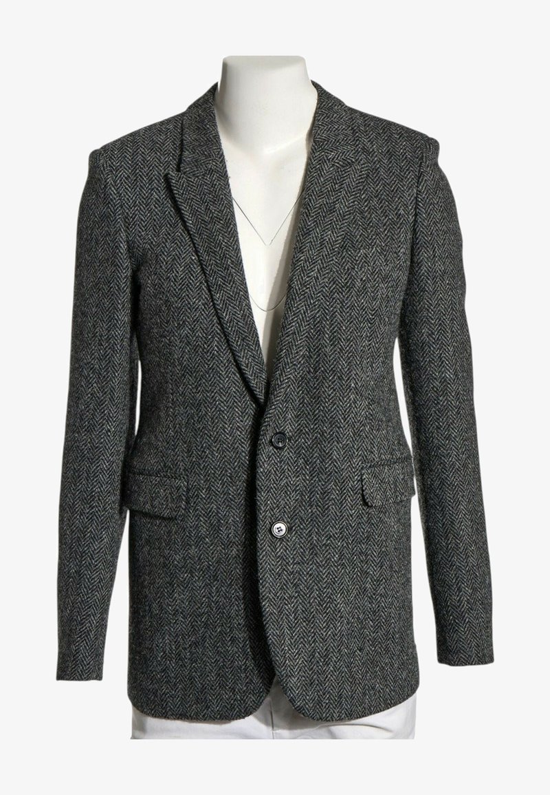 Blazer gris foncé à motif chevrons avec deux boutons, cols crantés et poches avant à rabat sur un buste de mannequin blanc.