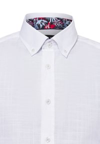 Weißes Hemd mit Knöpfen aus strukturiertem Stoff. Der Kragen weist ein kontrastierendes Blumenmuster in Rot, Blau und Schwarz auf. Sechs Knöpfe.