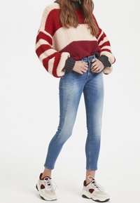 Maglione lavorato a maglia con texture a righe rosse e crema, jeans skinny blu a vita alta e sneakers grigie, bianche e bordeaux con lacci.