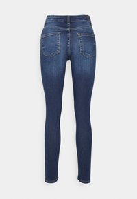 Calças skinny azul-escuro com uma textura suave, dois bolsos traseiros e detalhe de costura. Design ajustado afunilando nos tornozelos.