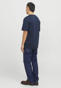 Navyblauwe katoenen T-shirt met korte mouwen, gecombineerd met donkerblauwe jeans en bruin veterschoenen. Eenvoudig ontwerp, relaxte pasvorm, geen patronen.