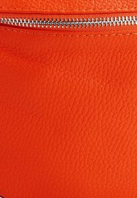 Orange textured leather material featuring a silver zipper at the top. The surface has a slightly pebbled finish.