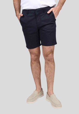 Shorts en coton bleu marine avec un devant plat et des poches latérales, accompagnés de chaussures à enfiler de couleur claire. Le tissu a une texture lisse.