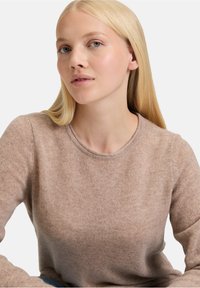 Beżowy sweter dzianinowy z okrągłym dekoltem i długimi rękawami, charakteryzujący się miękką fakturą i subtelnymi wariacjami kolorystycznymi w całej powierzchni.